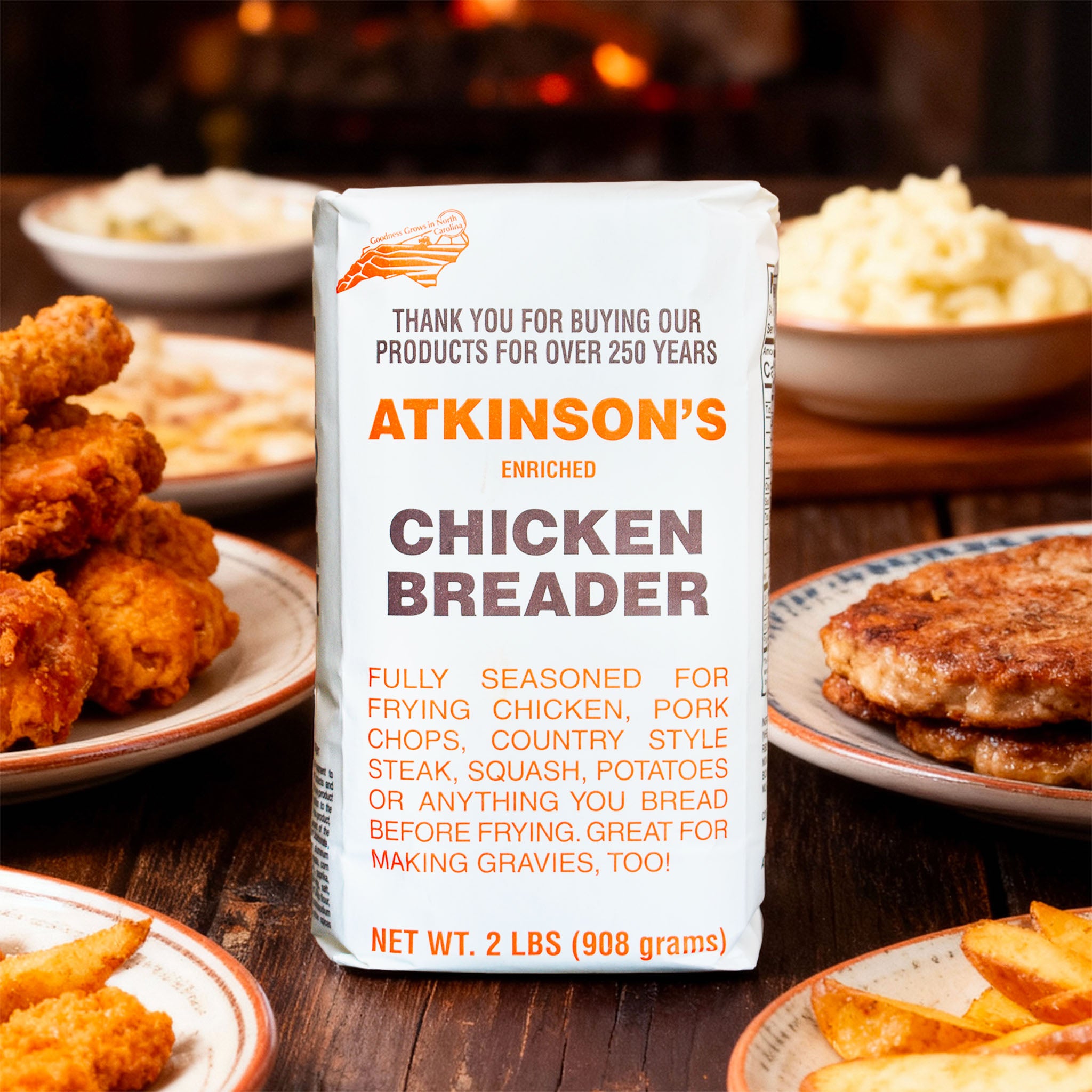 Atkinson's chicken breader 2 lb. bag on wooden table with fried chicken, country fried steak, mashed potatoes, and potato wedges.
