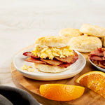 Breakfast setting with a biscuit sandwich, Suncrest Farms country ham, and orange slices on a wooden board.