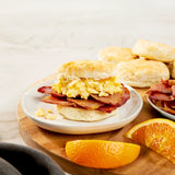 Breakfast setting with a biscuit sandwich, Suncrest Farms country ham, and orange slices on a wooden board.