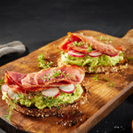 Two sandwiches with avocado, radishes, and Suncrest Farms country ham on a wooden cutting board.