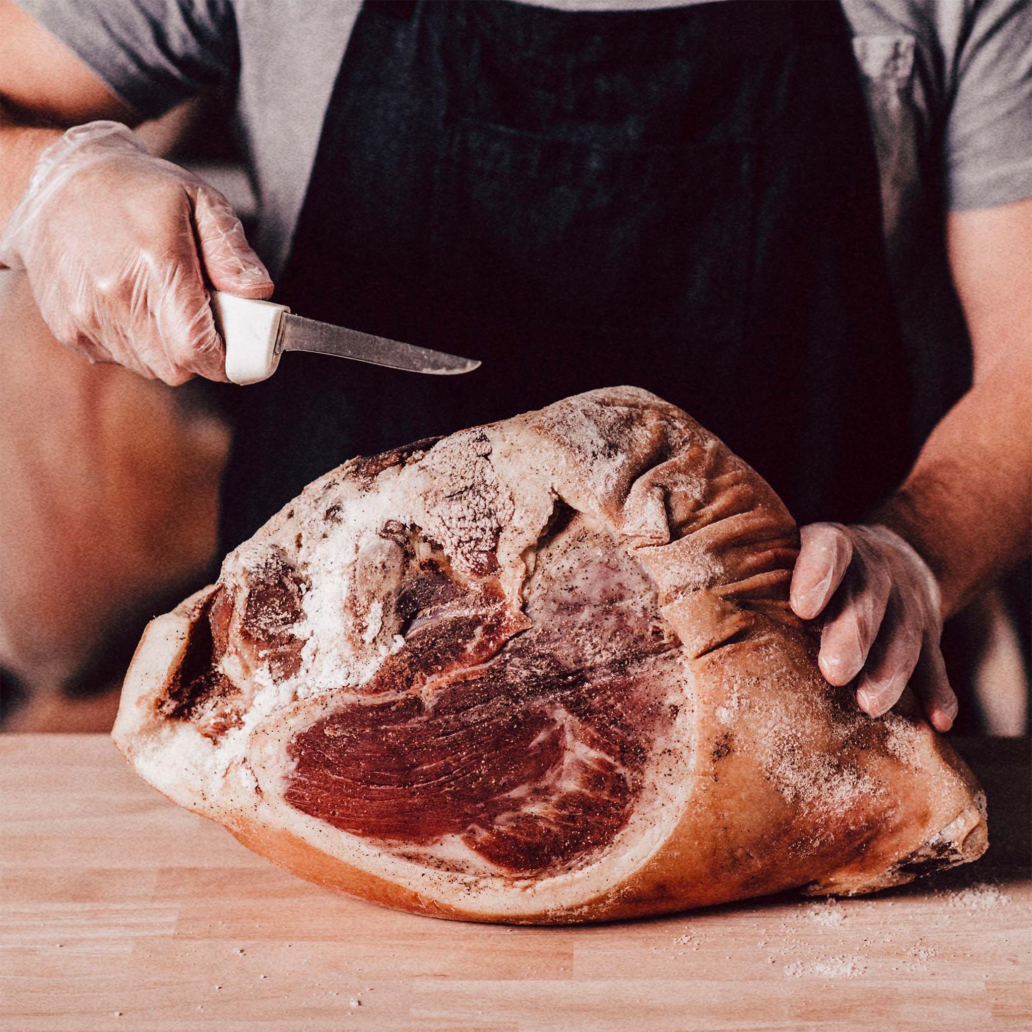 Man using Dexter boning knife to cut whole country ham on cutting board. 