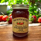 The Dutch Kettle homemade style amish strawberry jam on a wooden table with strawberries.