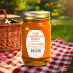 Jar of Dutch Kettle Amish Pure Mountain Honey on a checkered cloth with a picnic basket in the background.