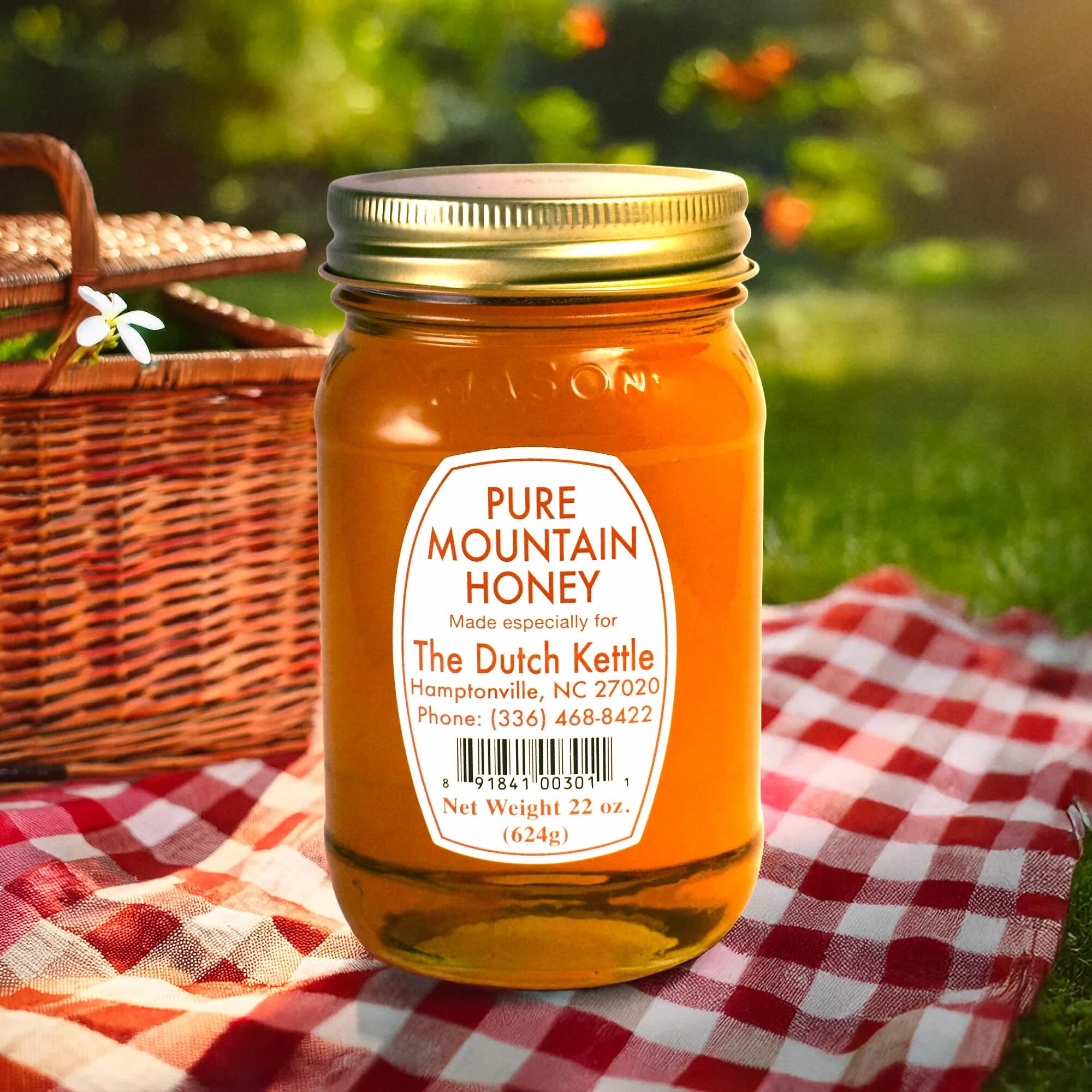 Jar of Dutch Kettle Amish Pure Mountain Honey on a checkered cloth with a picnic basket in the background.