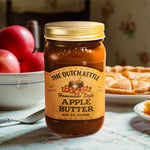 The Dutch Kettle Homemade Style Amish Apple Butter on a southern kitchen table with apple pie and apples in the background.