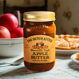 The Dutch Kettle Homemade Style Amish Apple Butter on a southern kitchen table with apple pie and apples in the background.