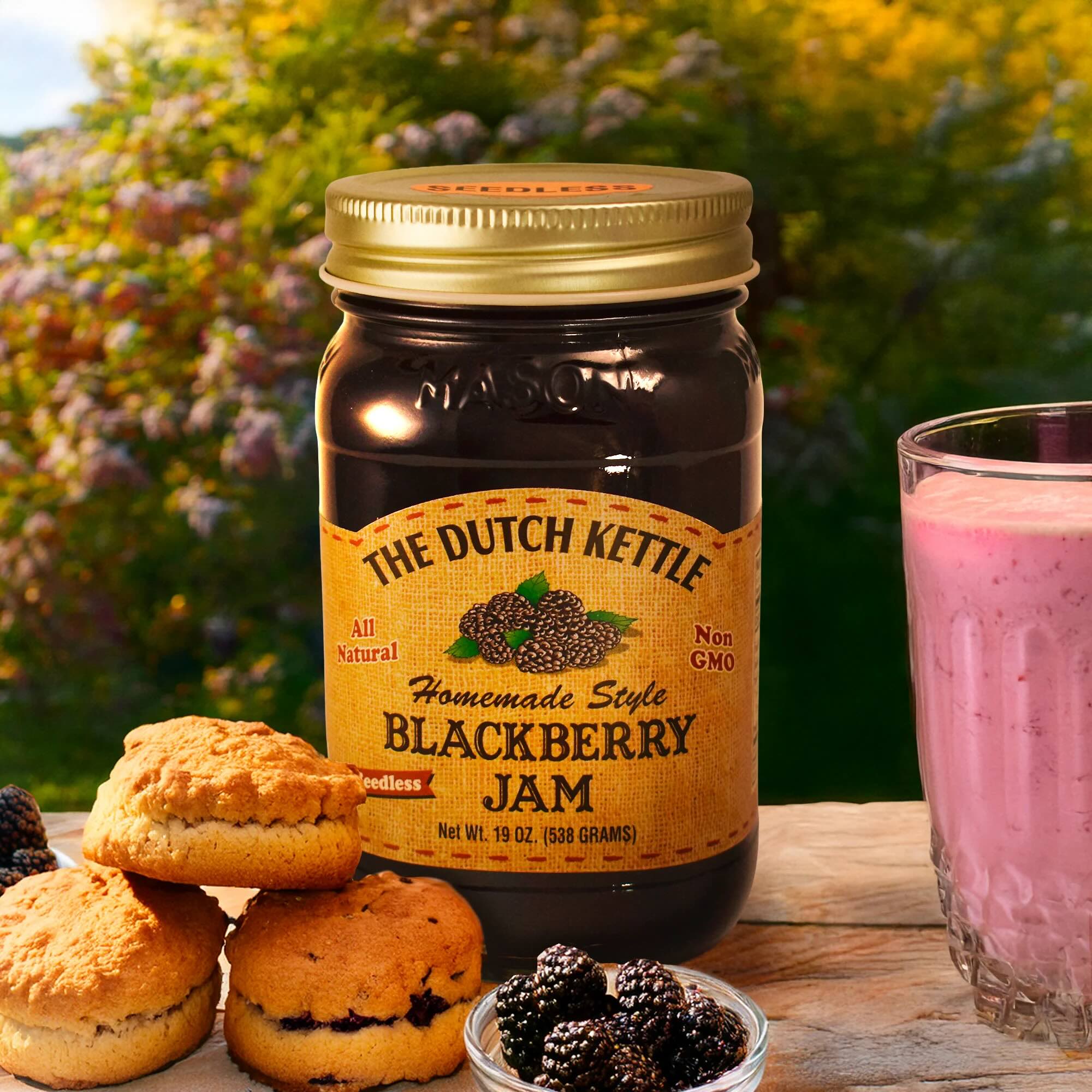 The Dutch Kettle Homemade Style Seedless Blackberry jam on wooden table with biscuits, blackberries, and a blackberry smoothie with a tree in the background. 