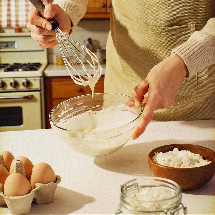 Person whisking ingredients in a bowl with eggs and flour on a kitchen counter.