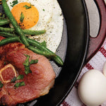 Suncrest Farms country ham, green beans, and an egg in a cast iron skillet on a tablecloth.