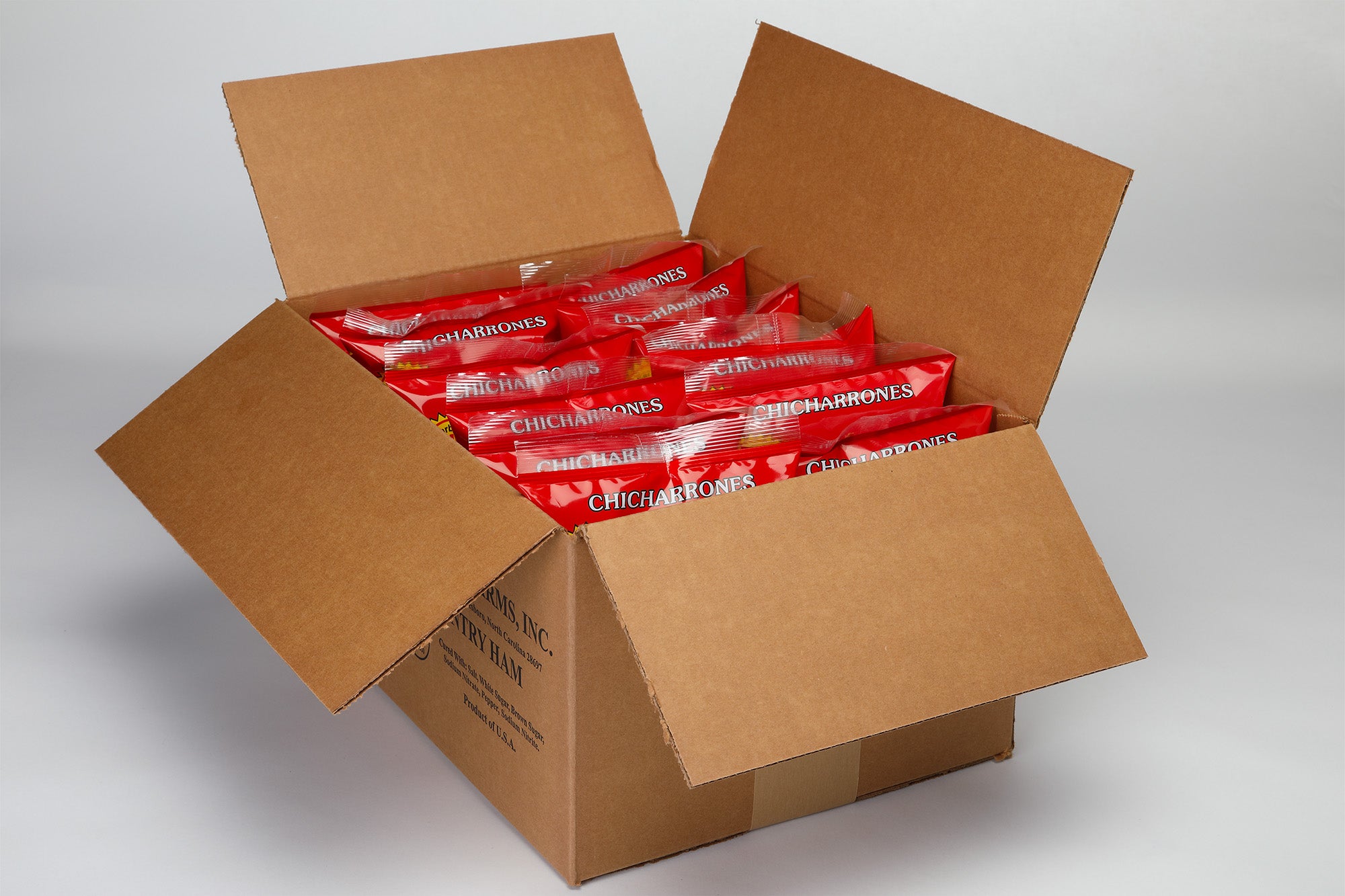 Cardboard box filled with 8 bags of Suncrest Farms hot flavor pork skins on a gray background.