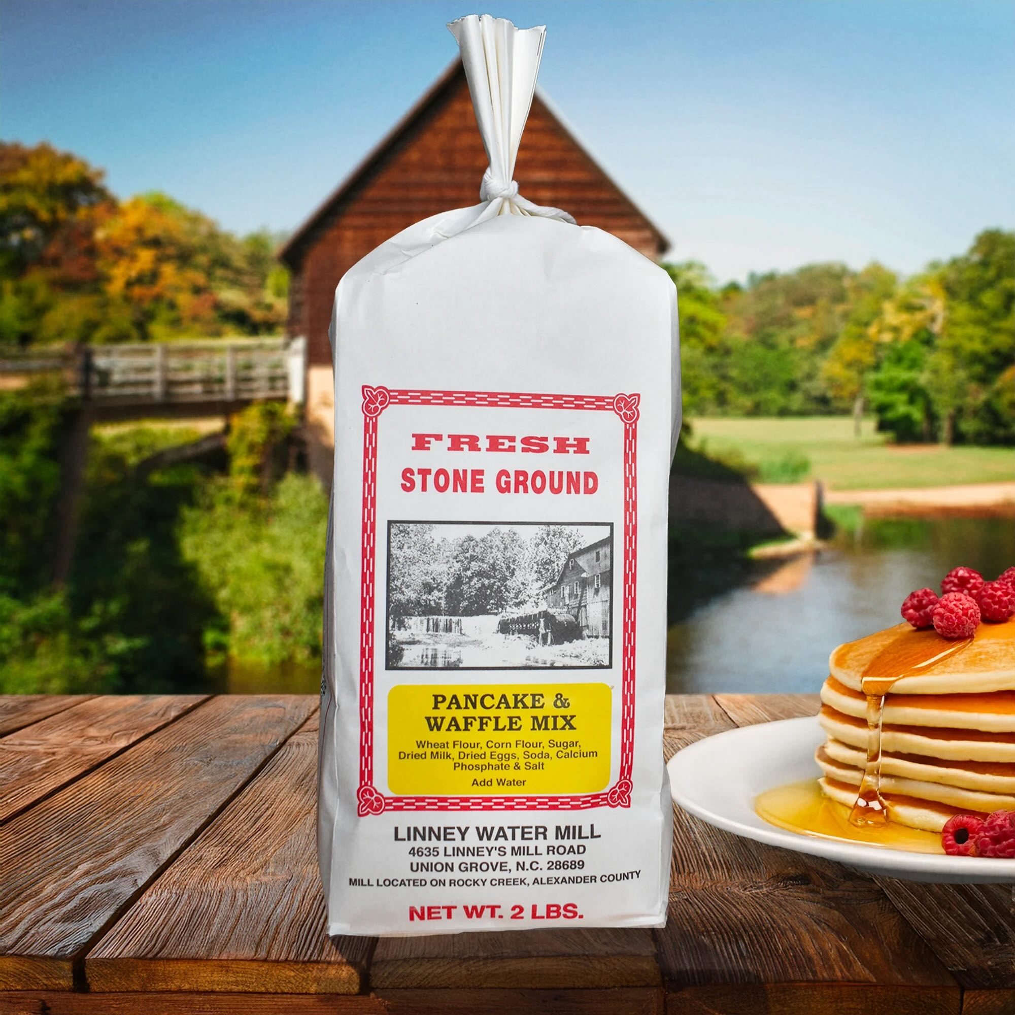 Linney Water Mill Stone Ground Pancake & Waffle Mix on a wooden table with a scenic country background.