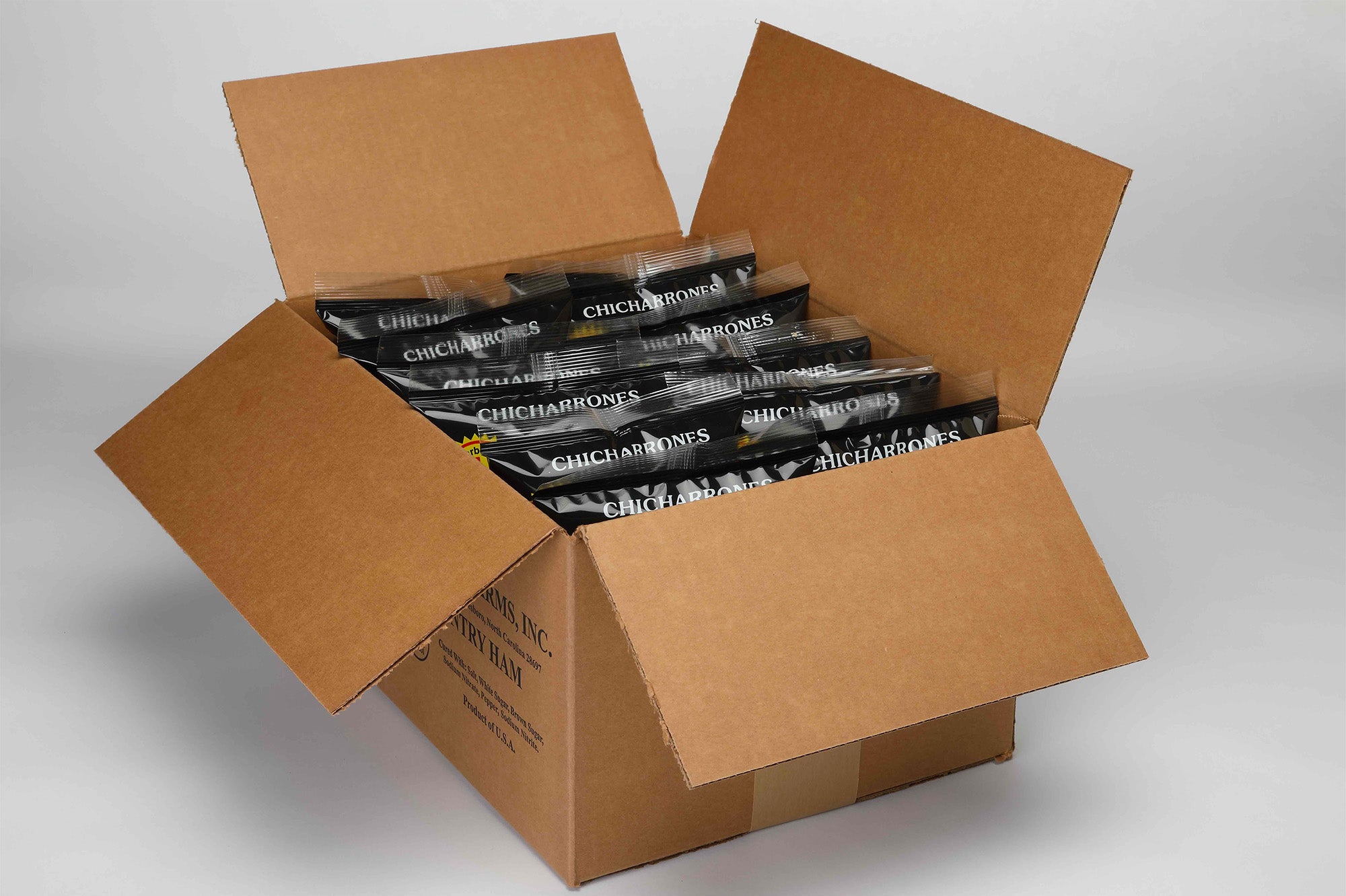 Open cardboard box containing 8 bags of Suncrest Farms Salt & Pepper Pork Skins. 