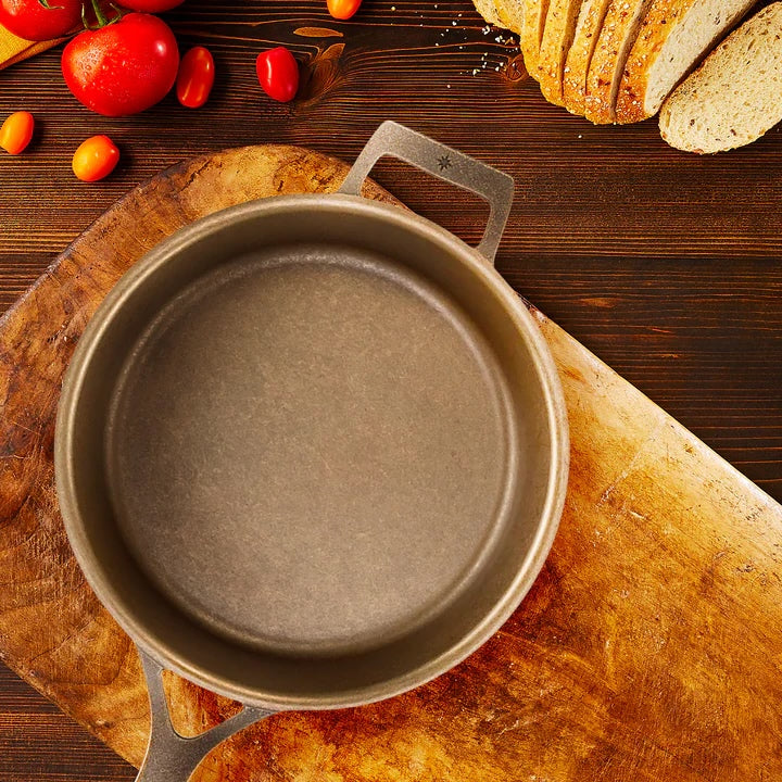 Cast iron skillet on a wooden cutting board with bread and tomatoes in the background.