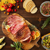 Wooden cutting board with Suncrest Farms sliced country ham, surrounded by vegetables and bread on a wooden table.