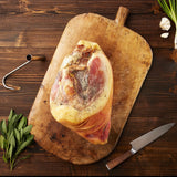 Suncrest Farms dry cured whole country ham on a wooden cutting board with herbs and a knife.