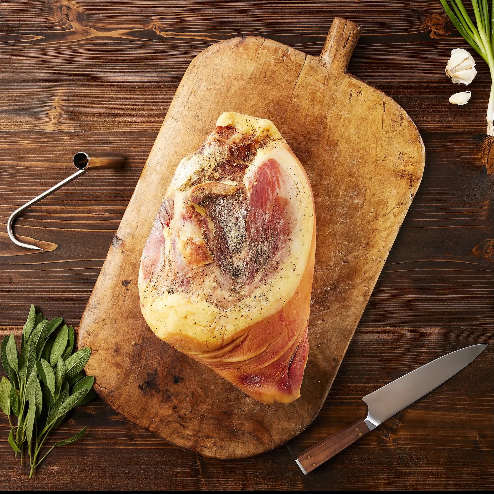 Suncrest Farms dry cured whole country ham on a wooden cutting board with herbs and a knife.